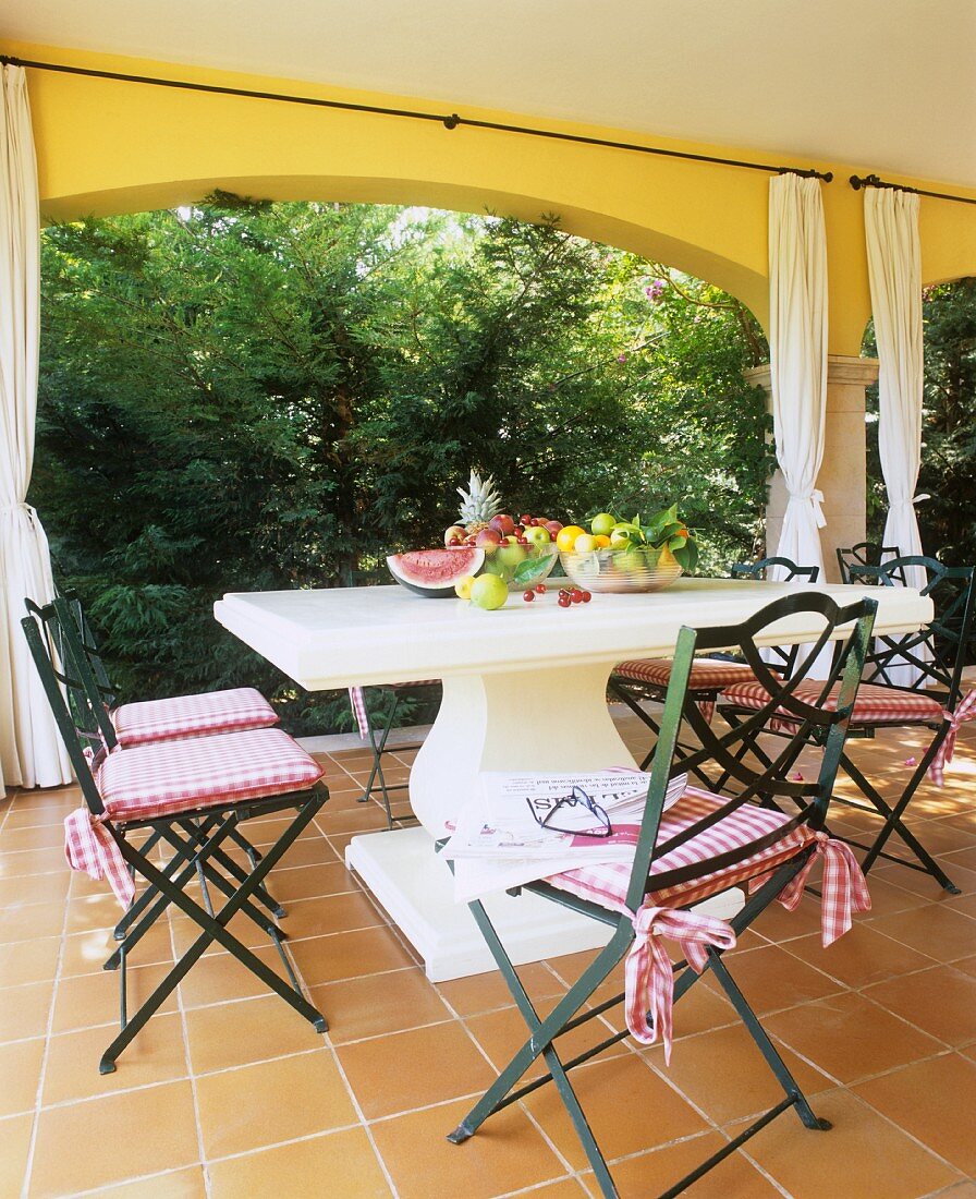 Various fruits on a stone table with a curved column foot and country house style chairs on a terrace