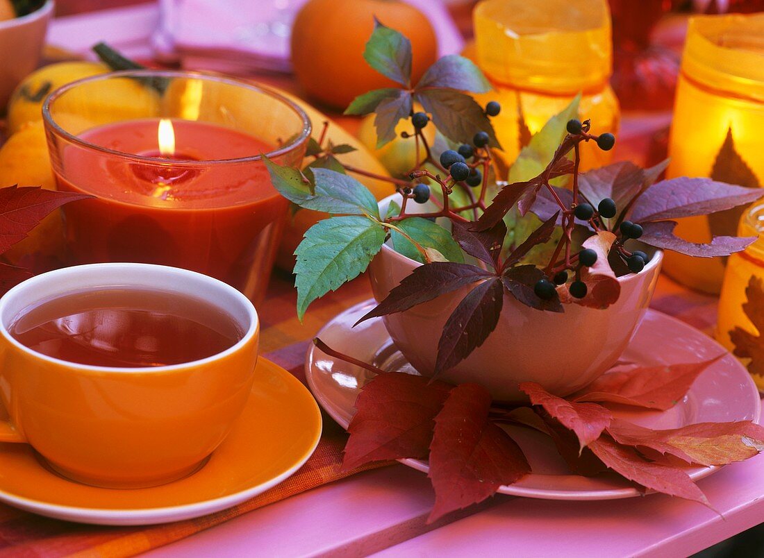 Eine Tasse Tee, Kerzenglas, Herbstlaub und Jungfernrebe