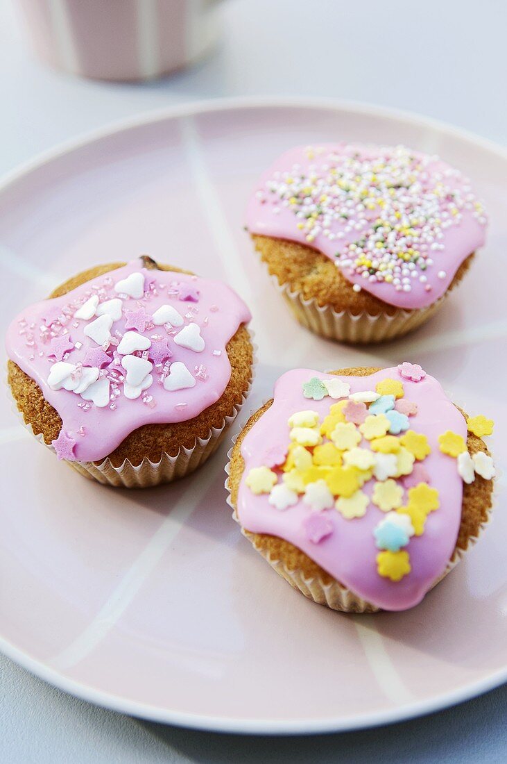 Three fairy cakes with pink icing and decorations