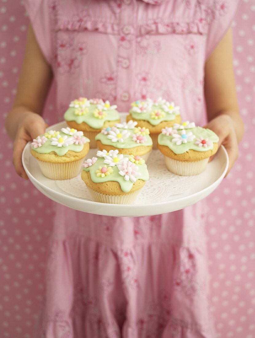 Mädchen hält Tablett mit verzierten Muffins