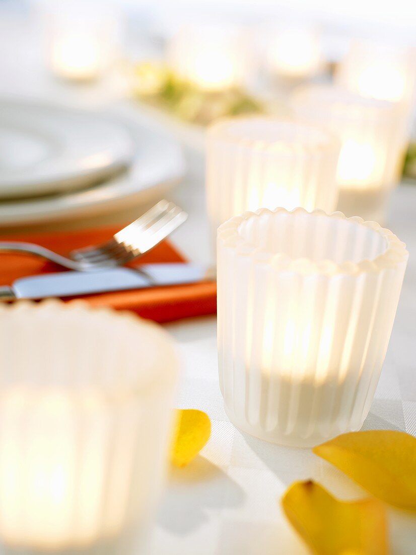 Teelichter in weissen Gläsern auf gedecktem Tisch