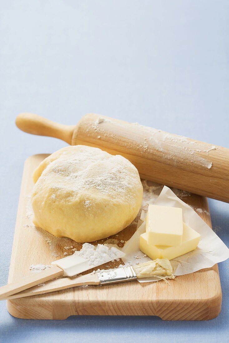 Ball of dough, butter and baking utensils on wooden board