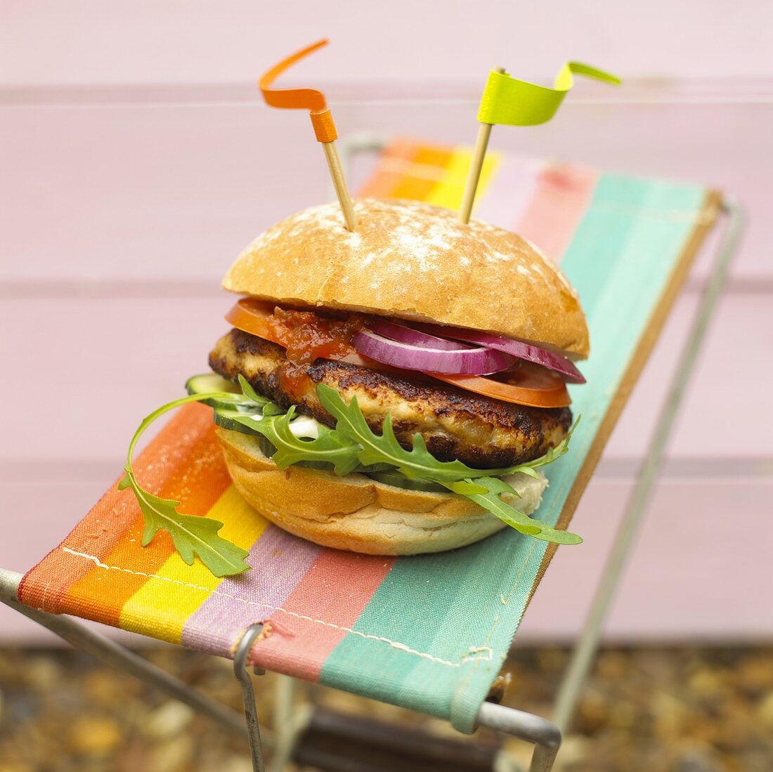 Chickenburger mit Zwiebeln und Rucola auf Campingstuhl