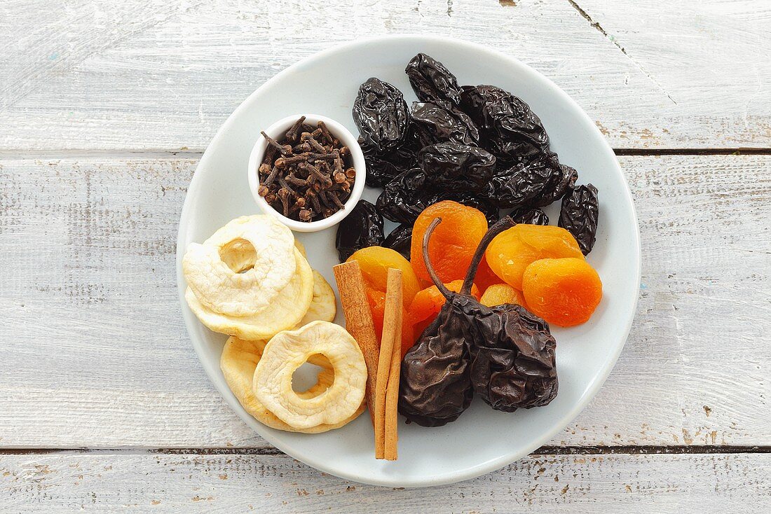 Assorted dried fruit, cinnamon sticks and cloves on plate