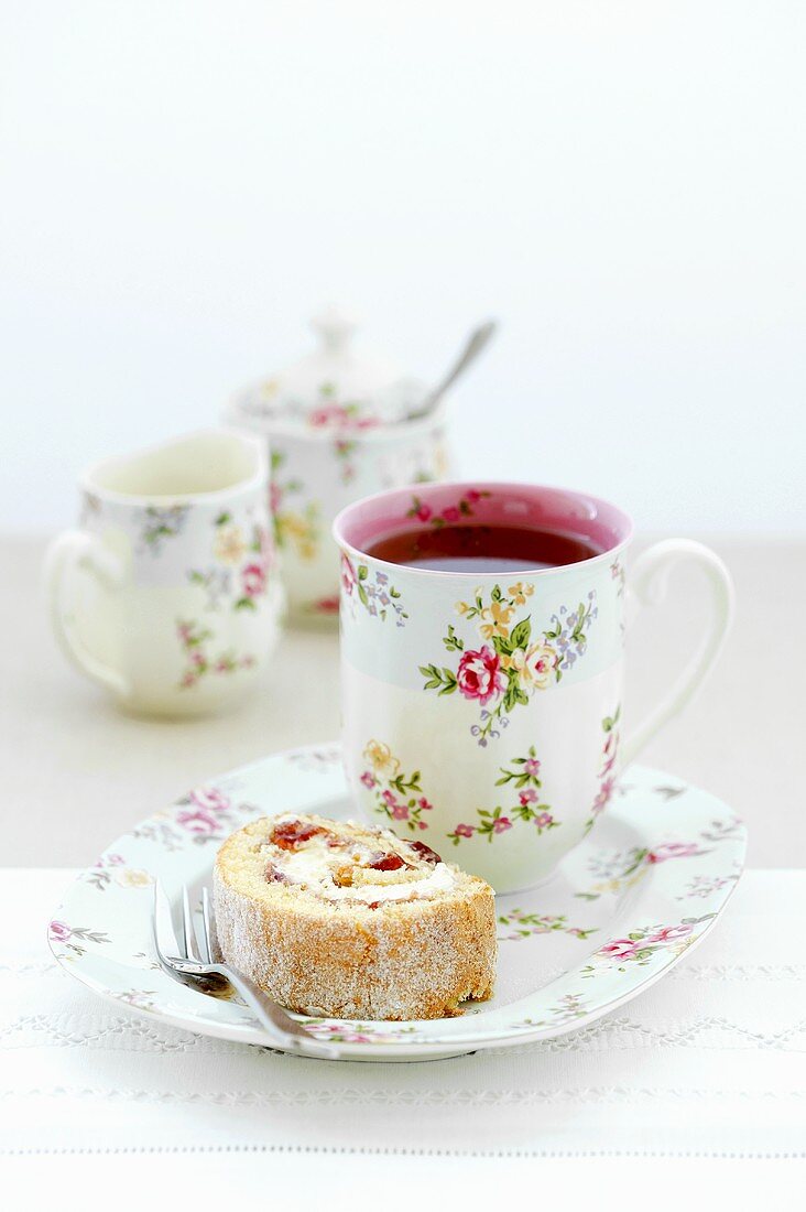 Piece of sponge roll with cream and jam filling and cup of fruit tea