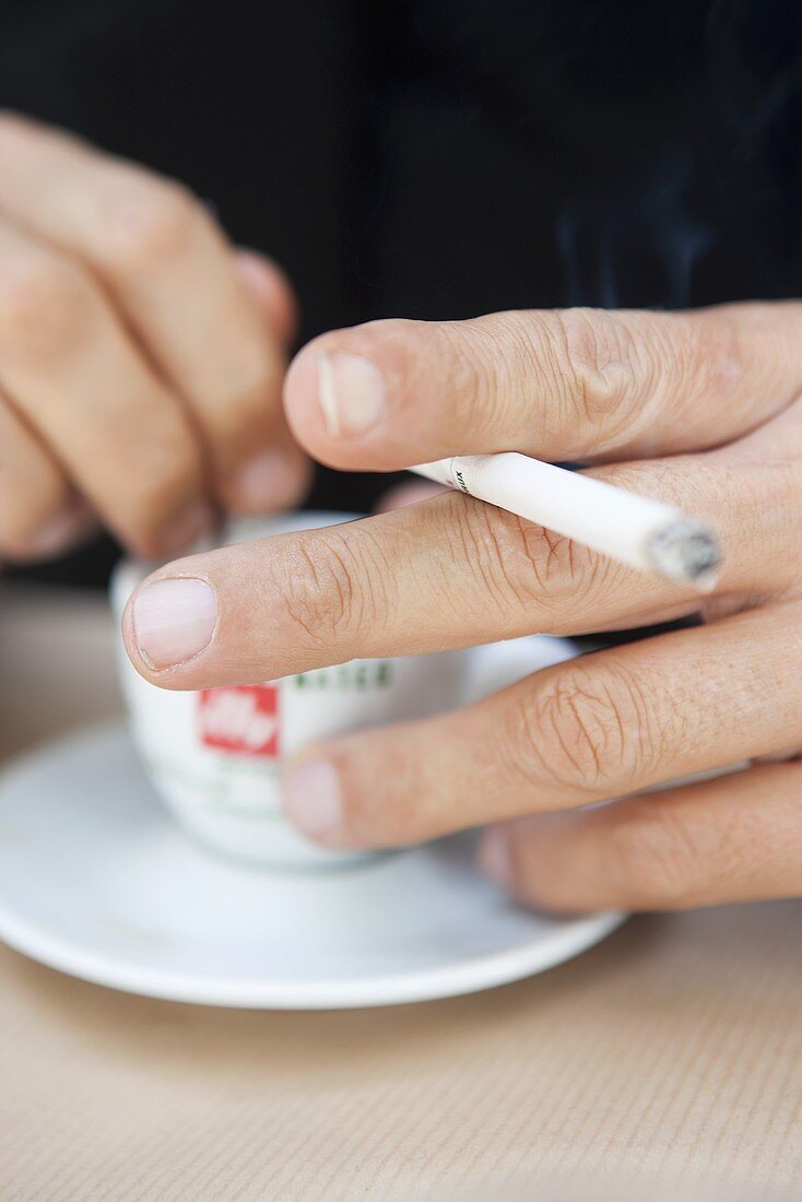 Hand holding a cigarette and a cup of espresso