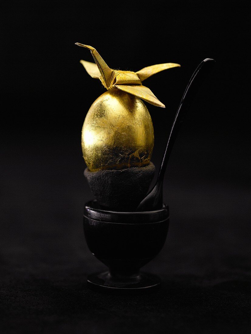 Goldenes Ei im Eierbecher vor schwarzem Hintergrund