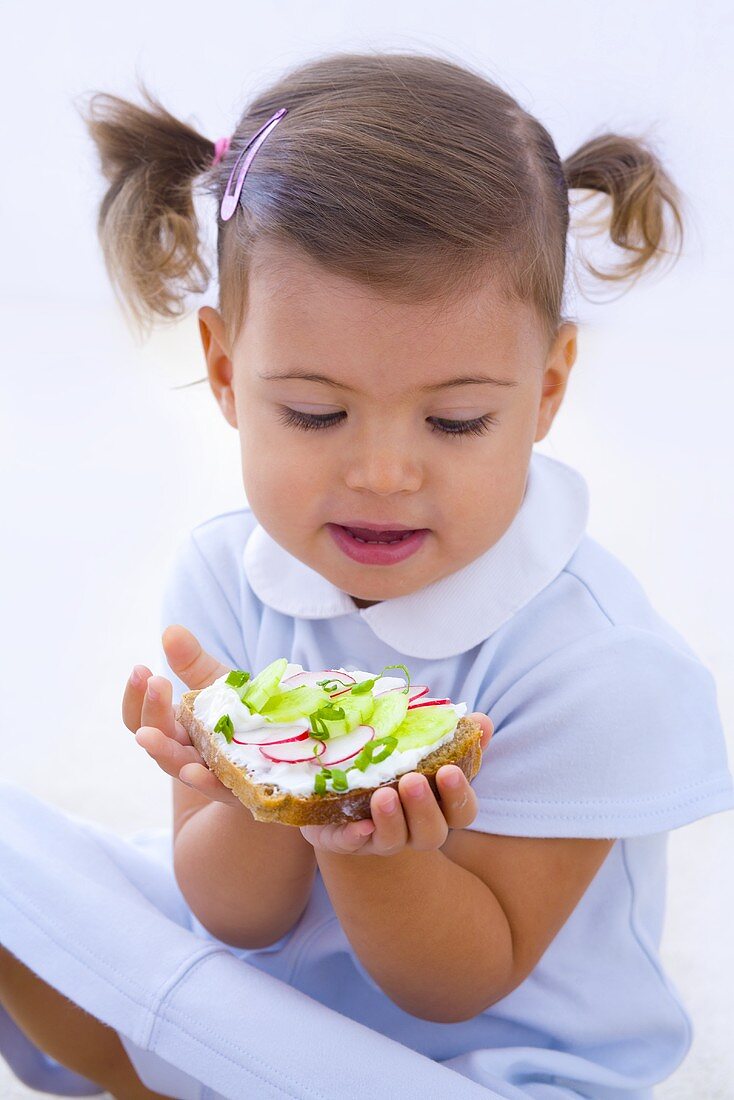 Kleines Mädchen hält Quarkbrot mit Gurken und Radieschen