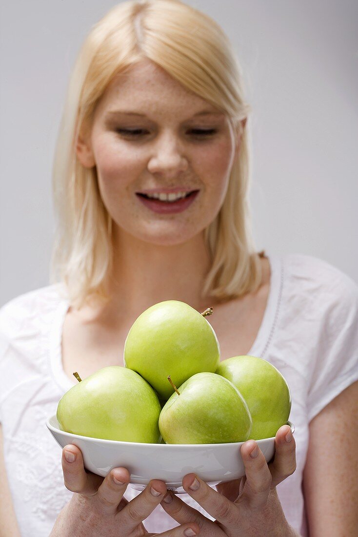 Blonde Frau hält Schale mit grünen Äpfeln