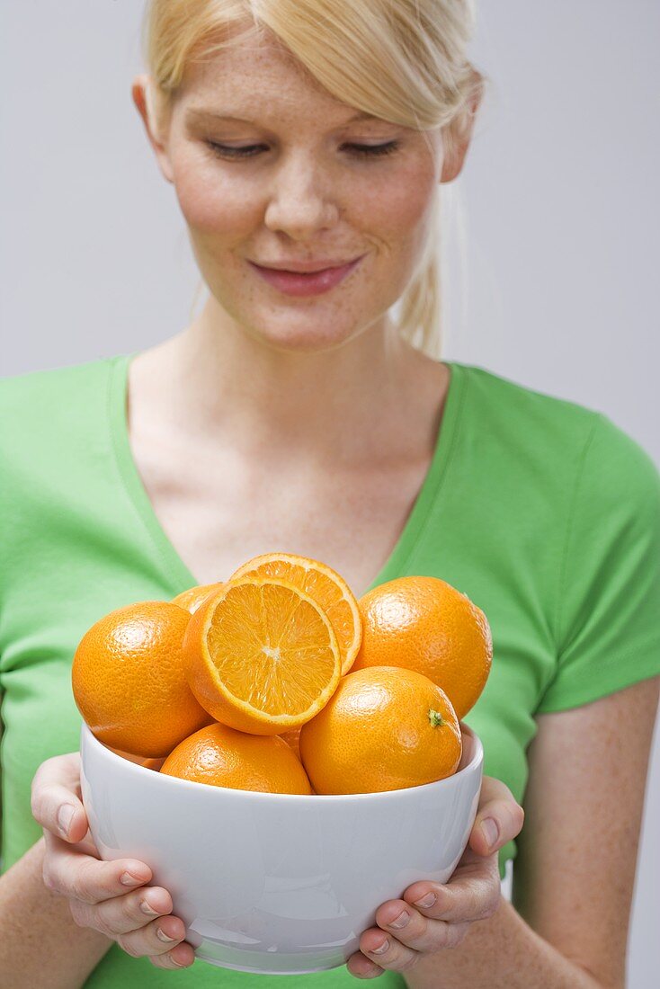 Woman holding bowl of fresh oranges