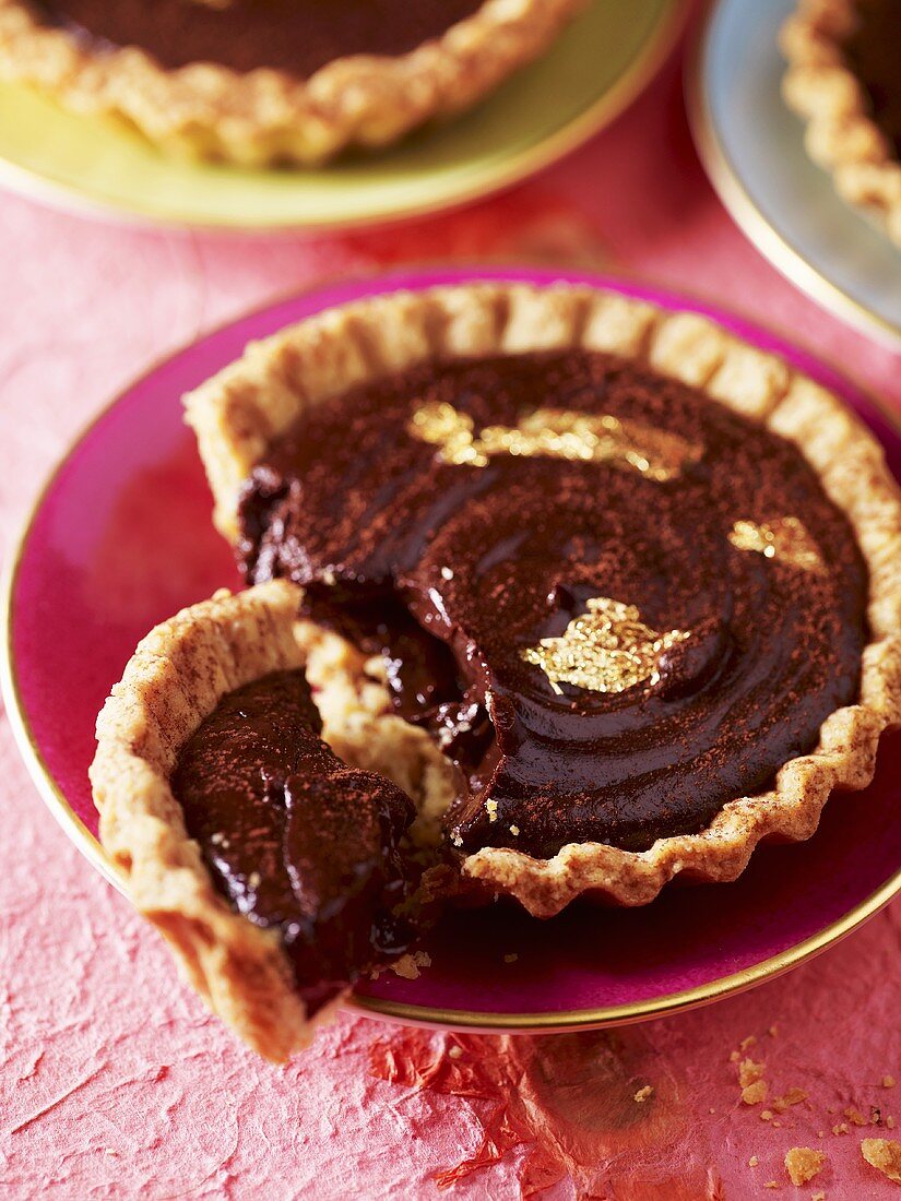 Small chocolate tart with gold leaf on gold-rimmed saucer