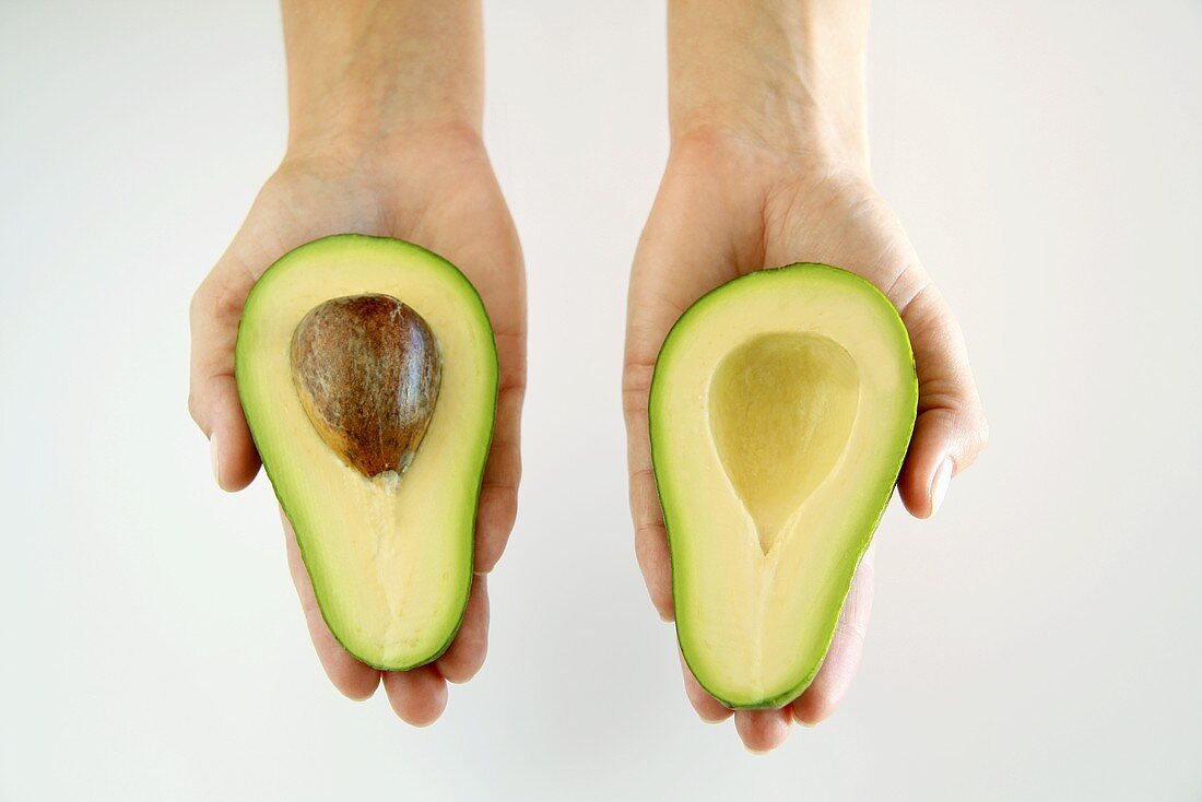 Hands holding two avocado halves