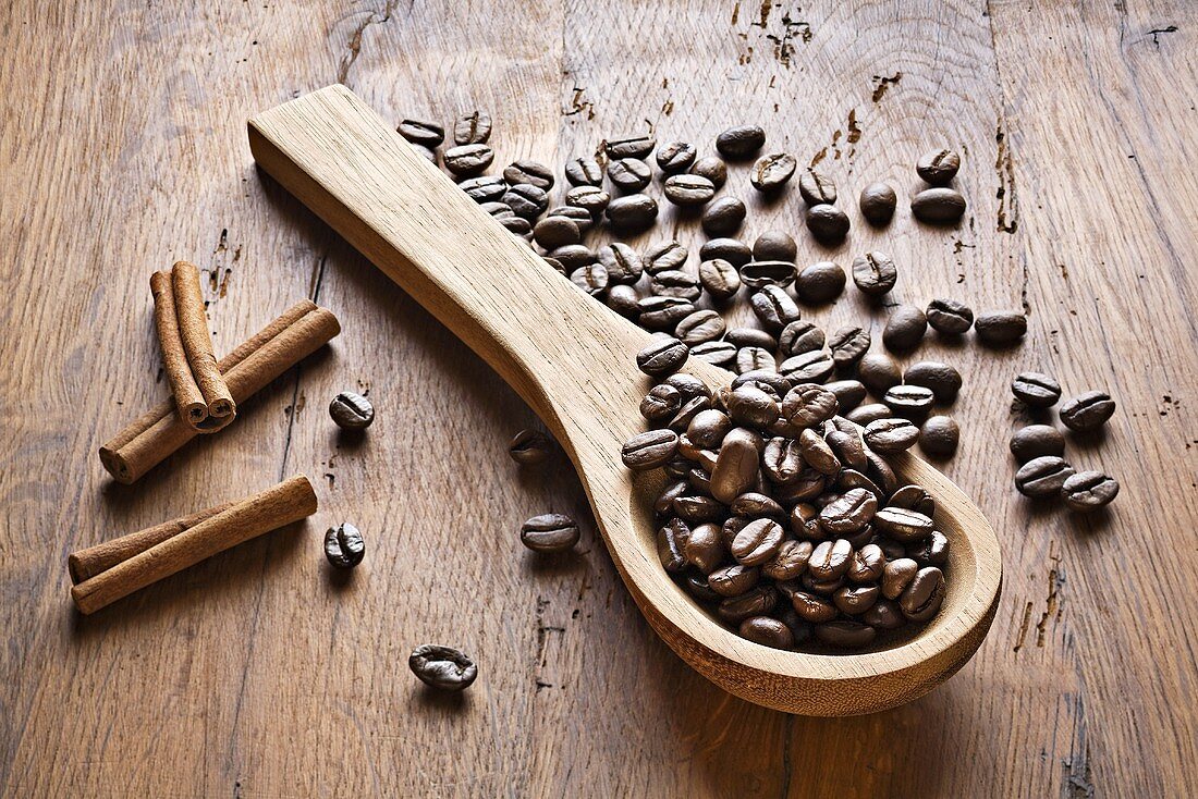 Kaffeebohnen, Holzlöffel und Zimtstangen auf Holzuntergrund