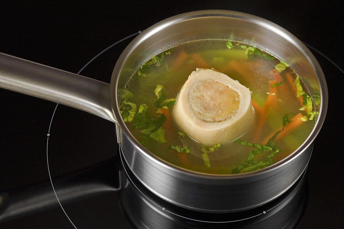 Clear broth with marrowbone and vegetables in pan
