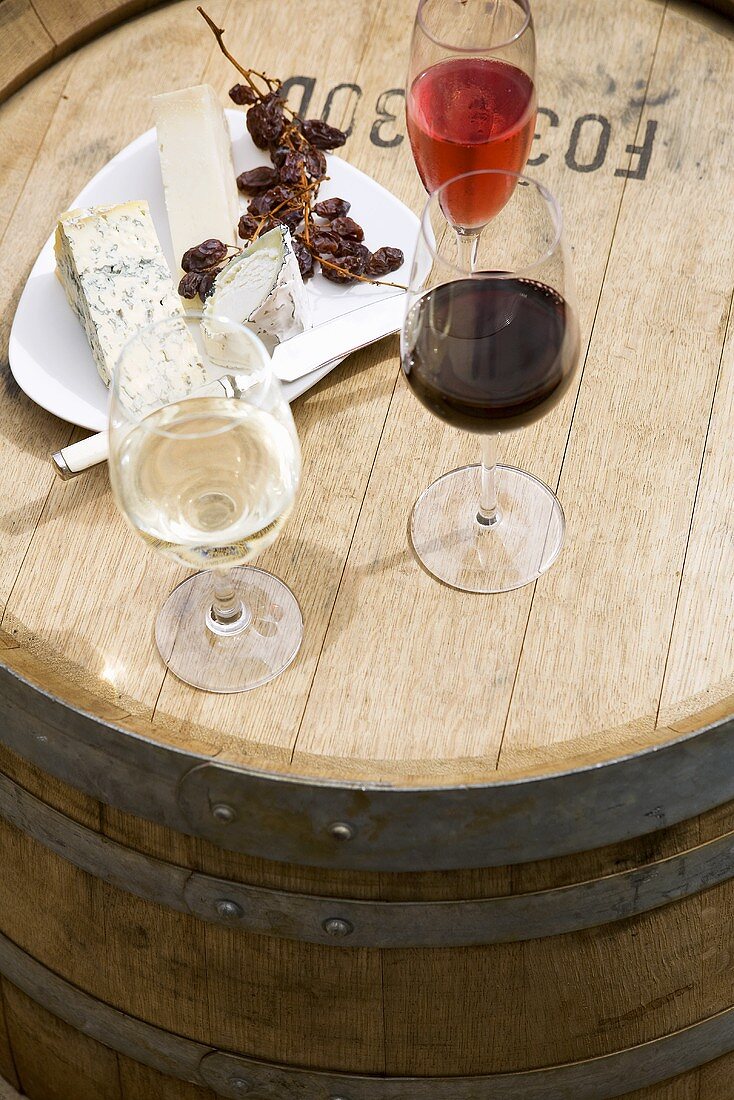 Weingläser, Käseplatte und Trauben auf Weinfass