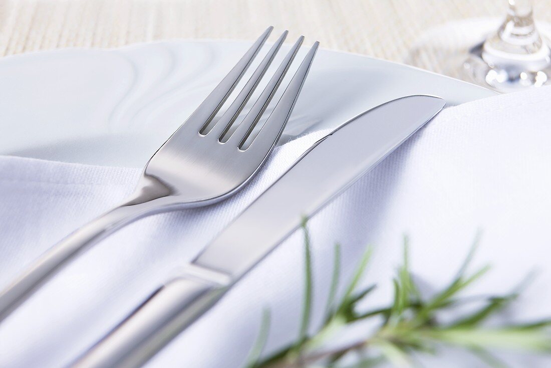 Knife and fork on fabric napkin with rosemary sprig