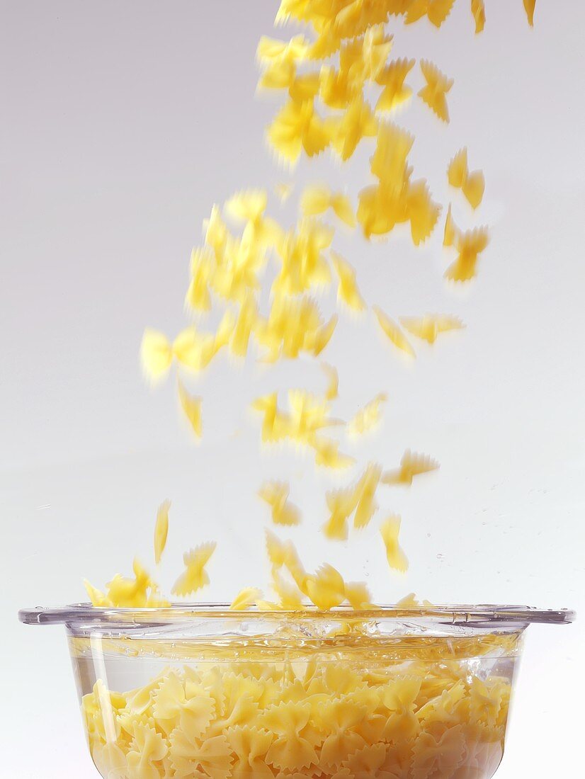 Farfalle falling into water in glass pot