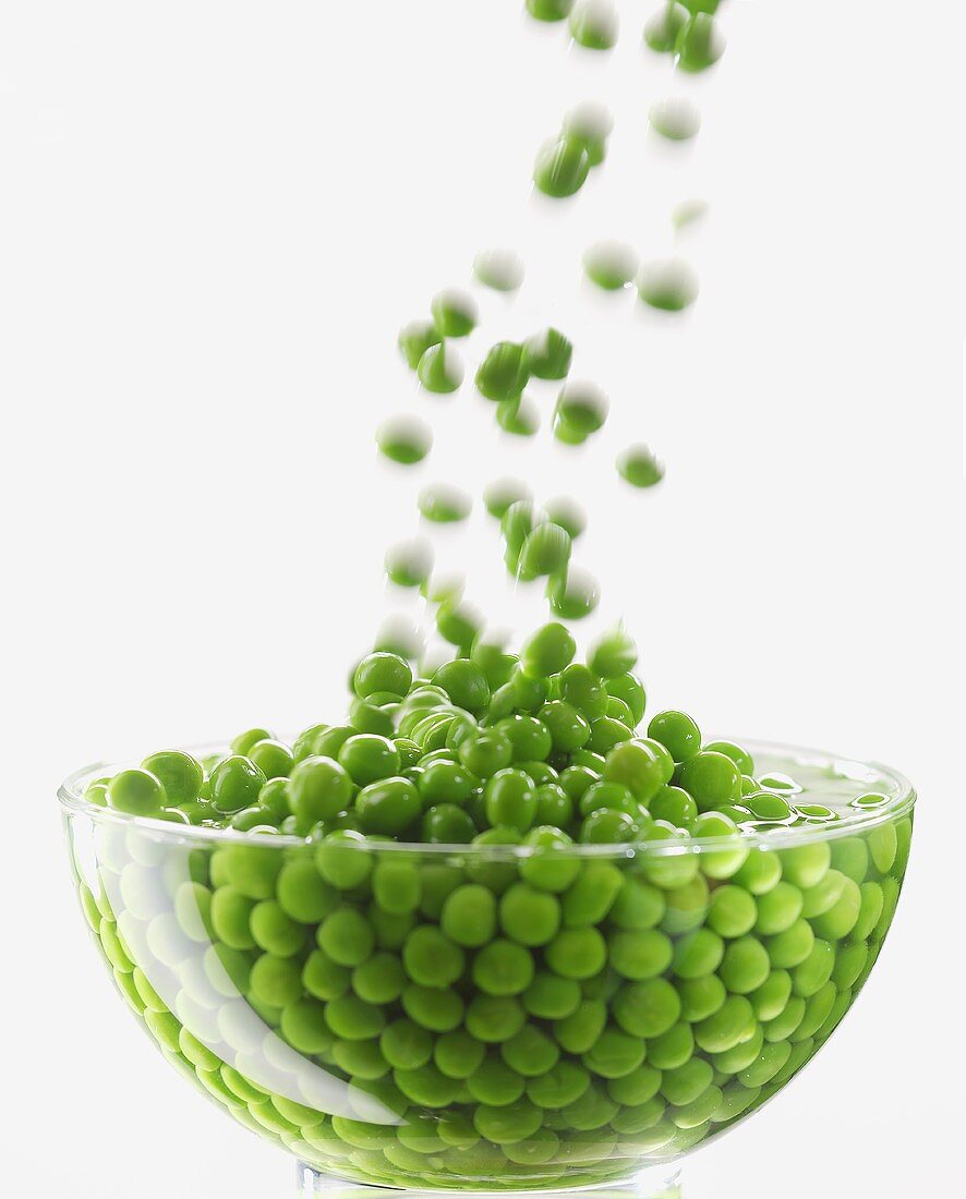 Peas falling into water in glass bowl