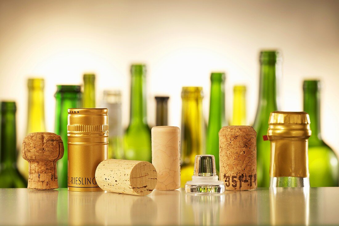 Diverse Weinflaschenverschlüsse, im Hintergrund Weinflaschen