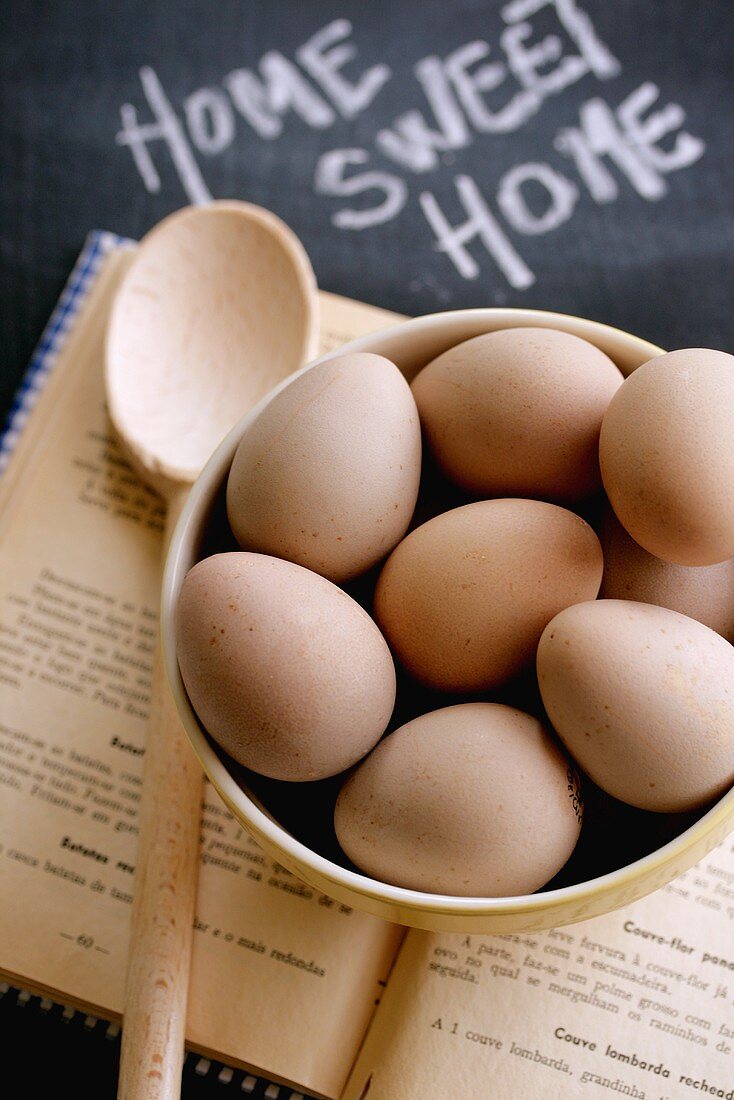 Fresh eggs in bowl on cookery book with wooden spoon