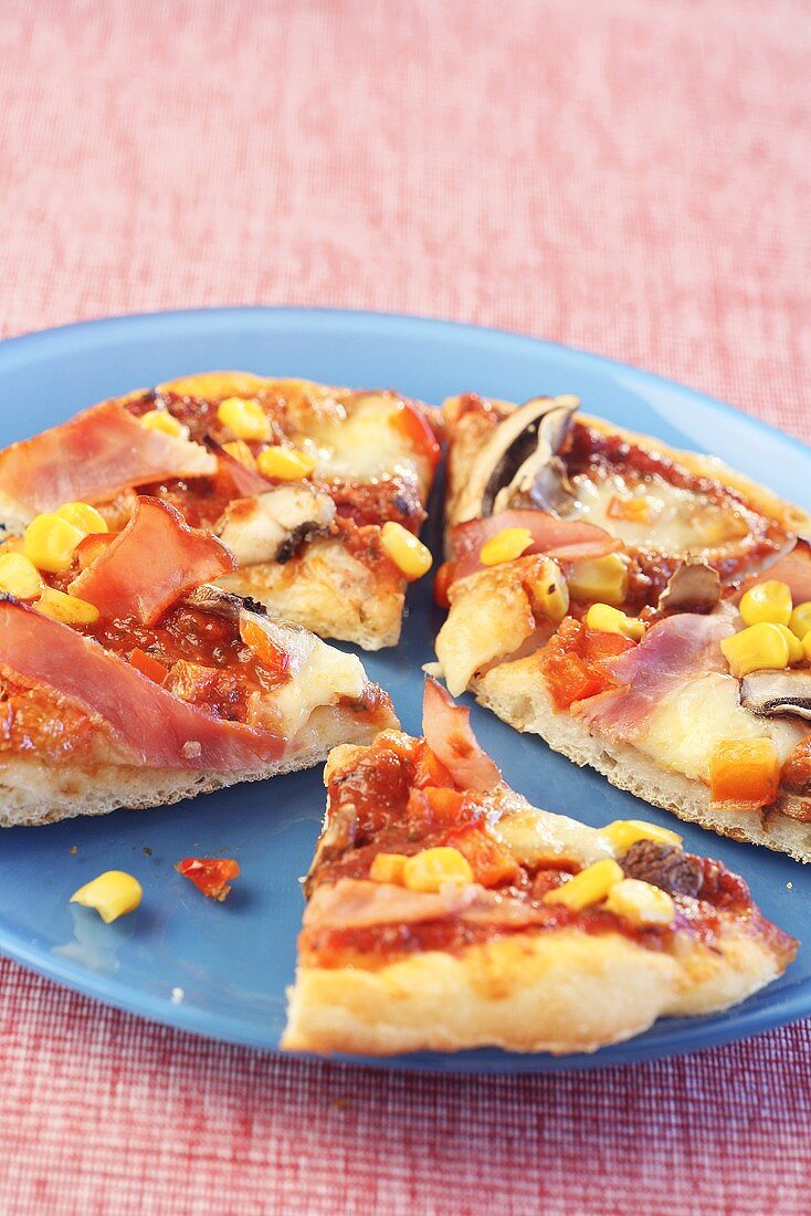 Four slices of pizza topped with ham, sweetcorn and mushrooms