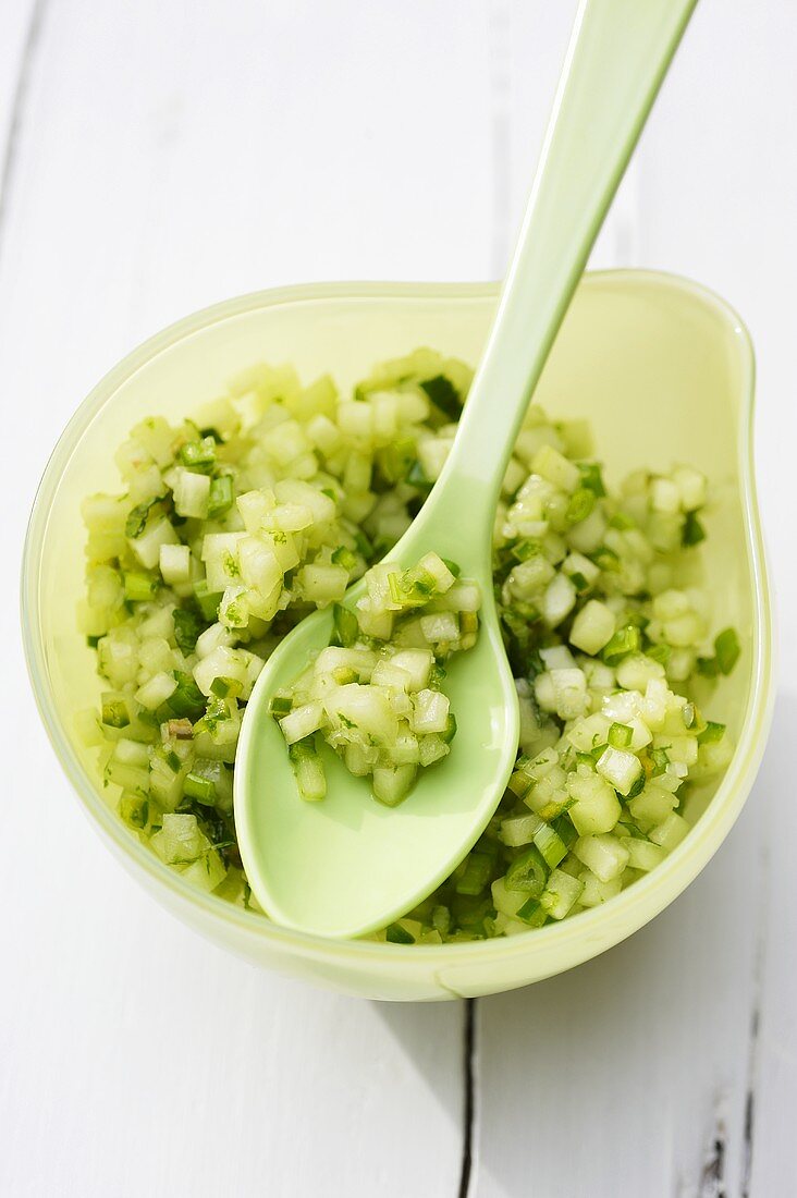 A bowl of cucumber salsa with a spoon