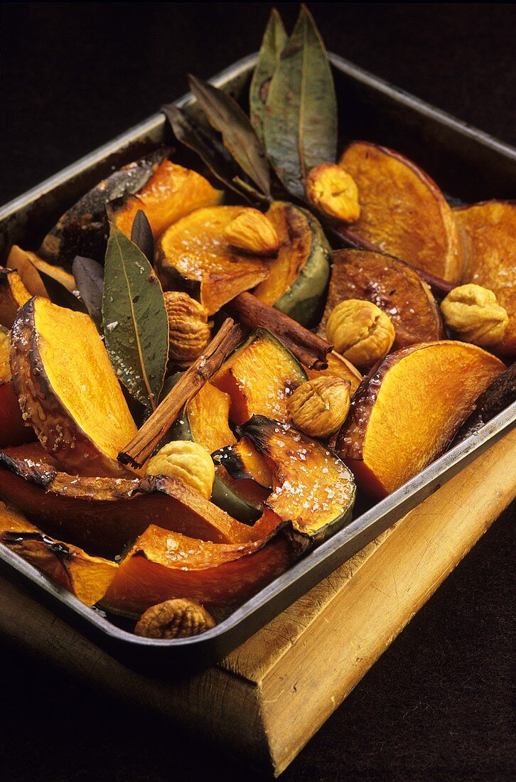 Pumpkin with chestnuts and cinnamon sticks in roasting tin