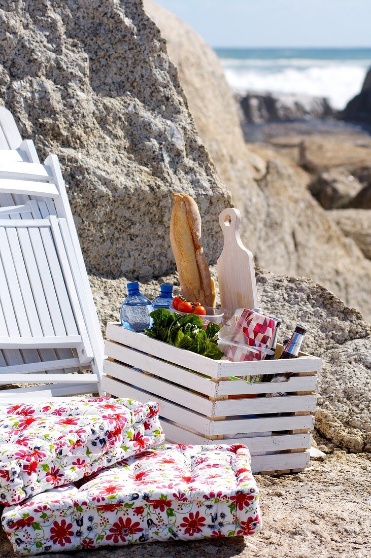 Kiste mit Lebensmitteln, Liegestühle und Sitzkissen am Felsen