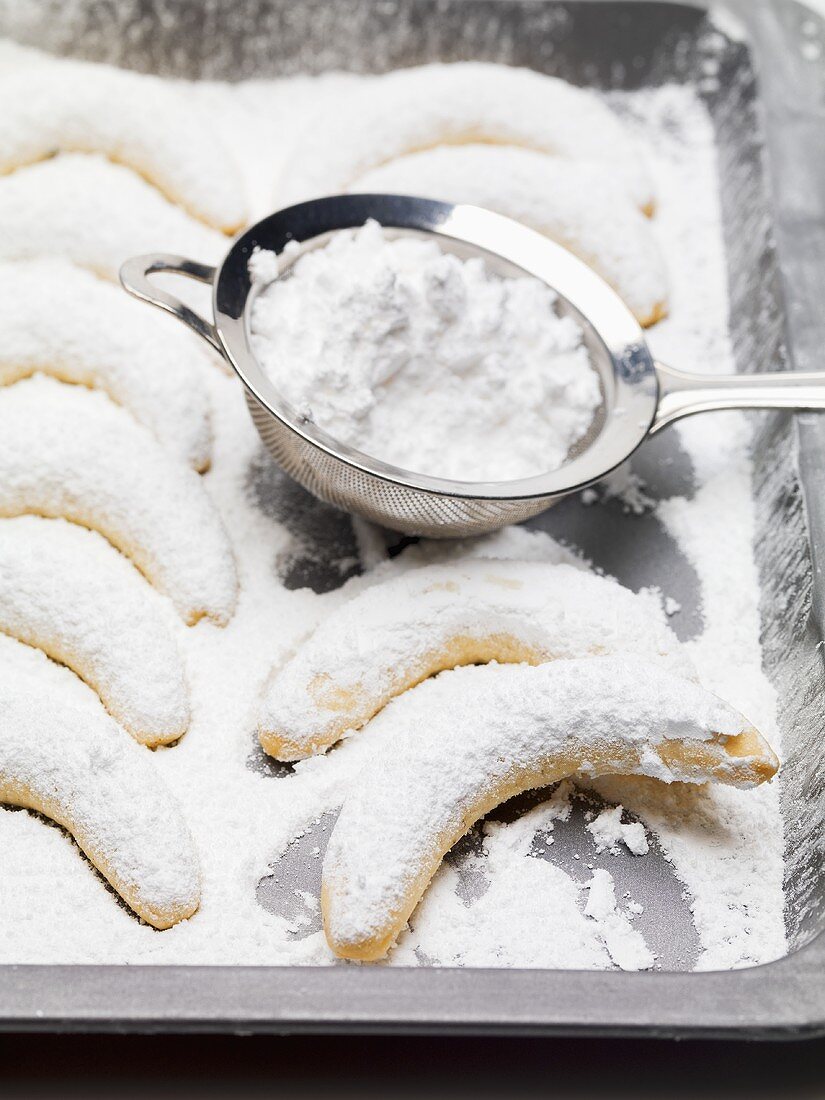Vanilla crescents with icing sugar and sieve on baking tray