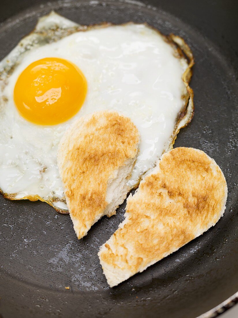 Fried egg and broken toast heart in frying pan