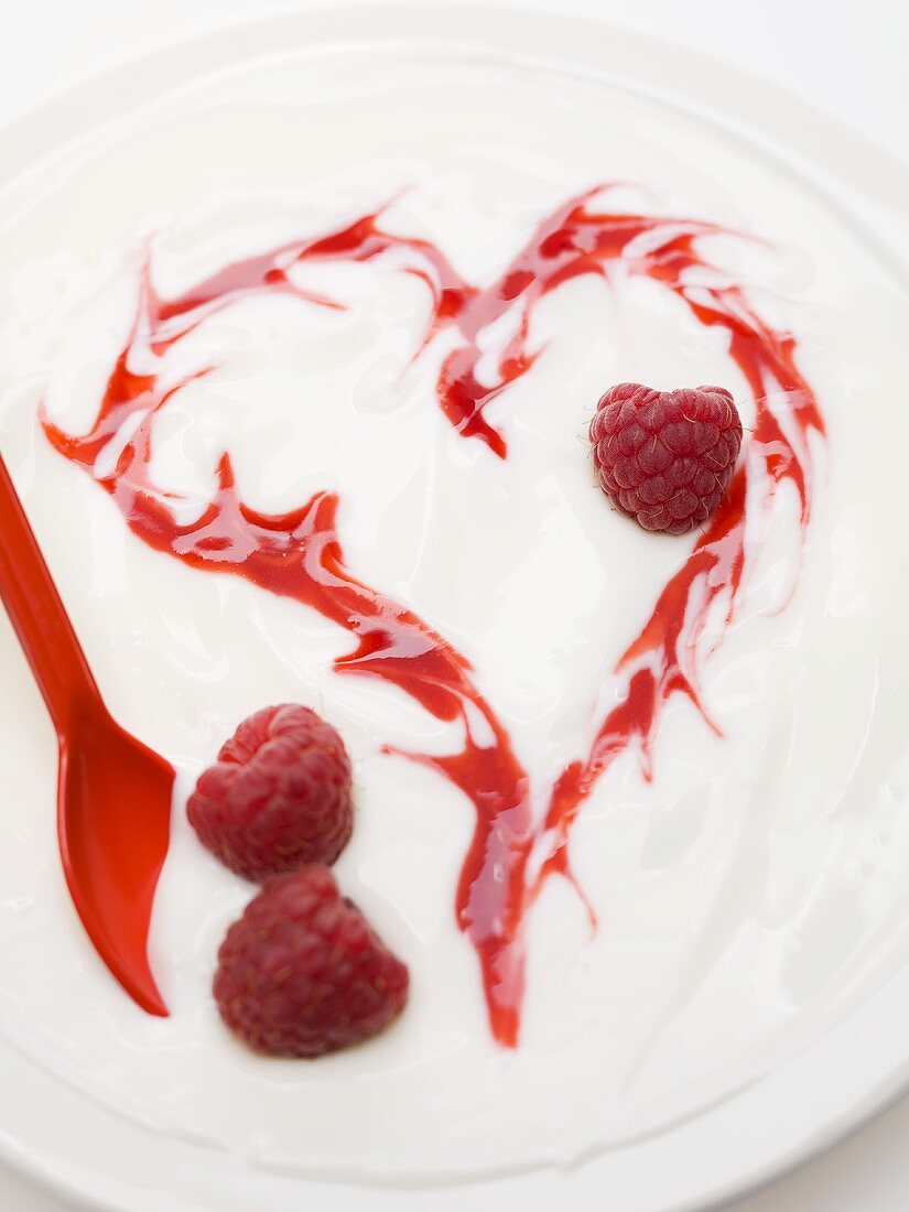 Yoghurt with raspberries and heart drawn in raspberry sauce