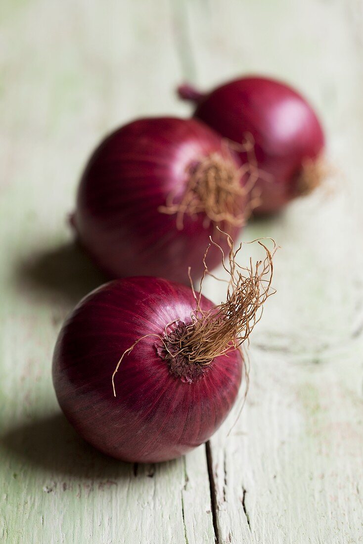 Three red onions on wooden background