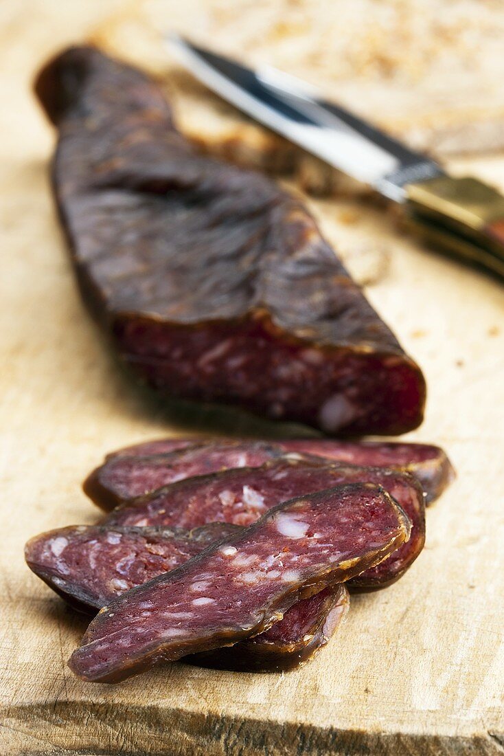 Goat salami on wooden board with knife