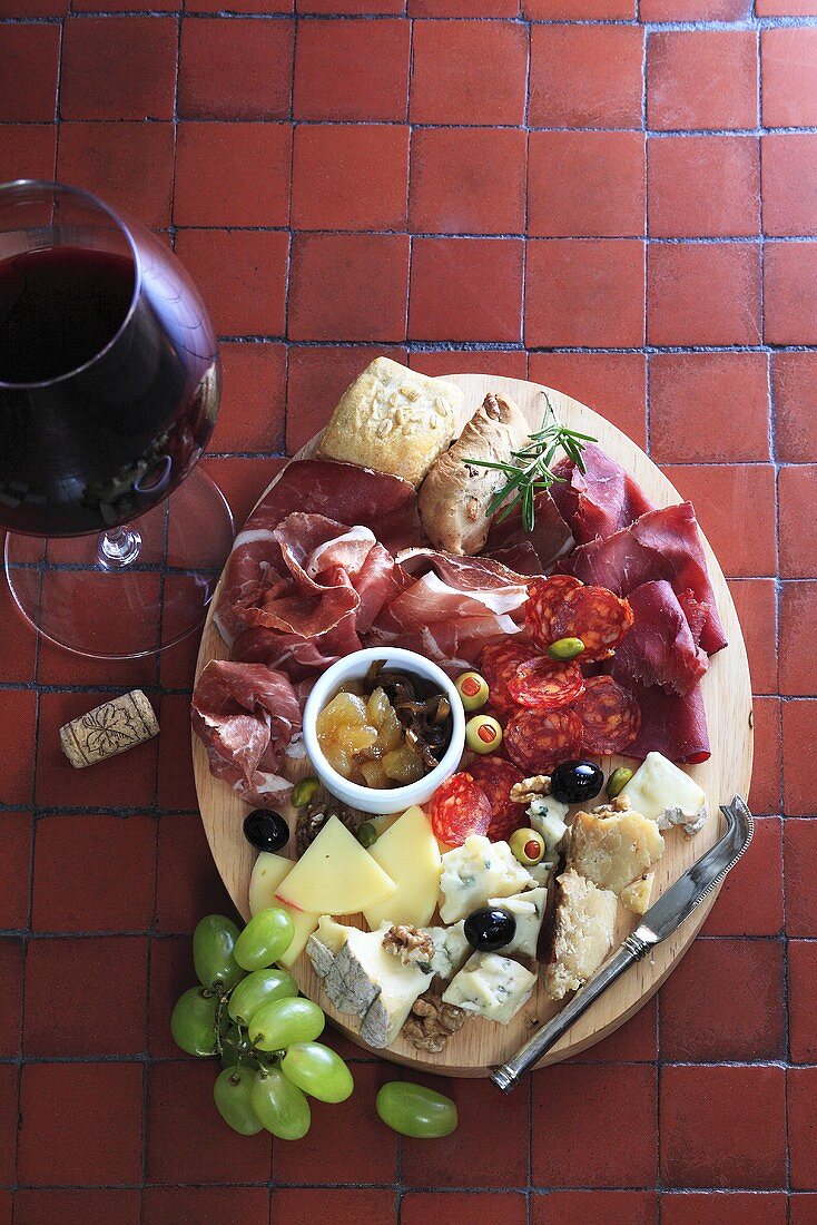 Antipasti platter with sausage and cheese, glass of red wine