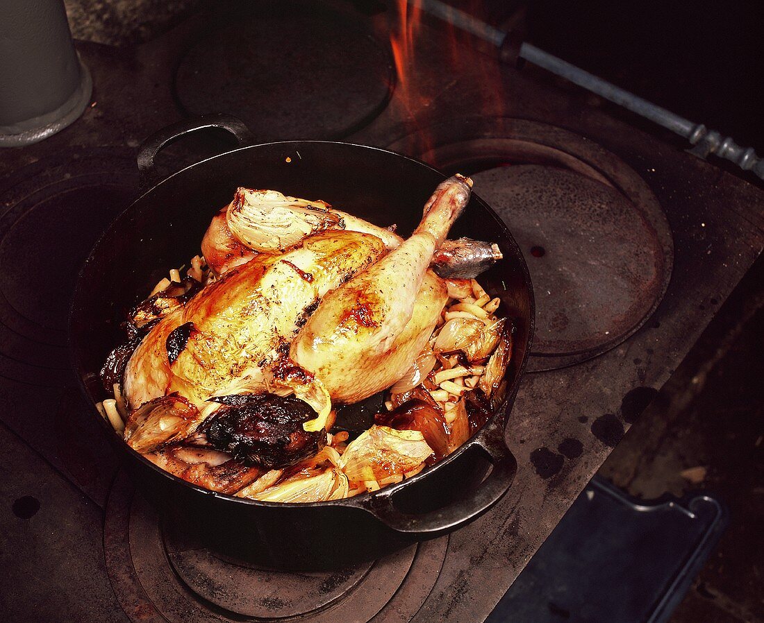 Bresse chicken on onions, tomatoes and macaroni in cast-iron pan