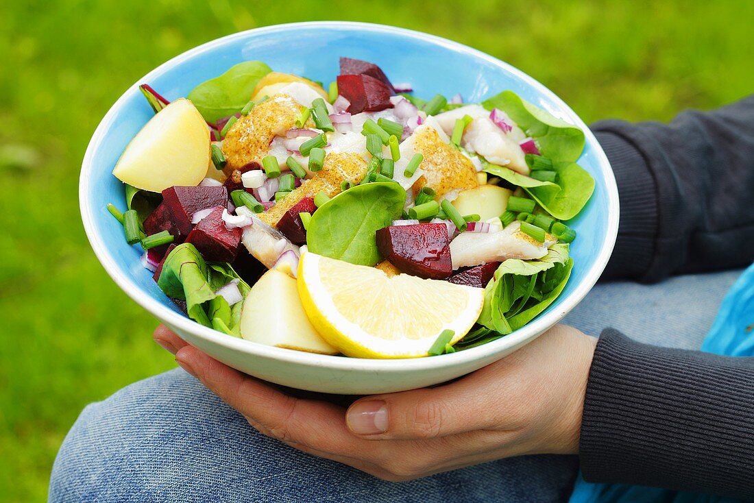 Person holding bowl of salad (beetroot, herring, potatoes)