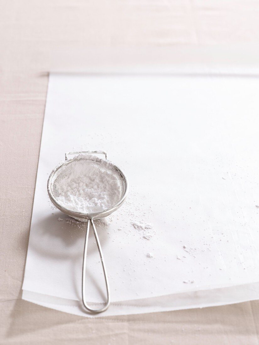 Sieve full of icing sugar on paper