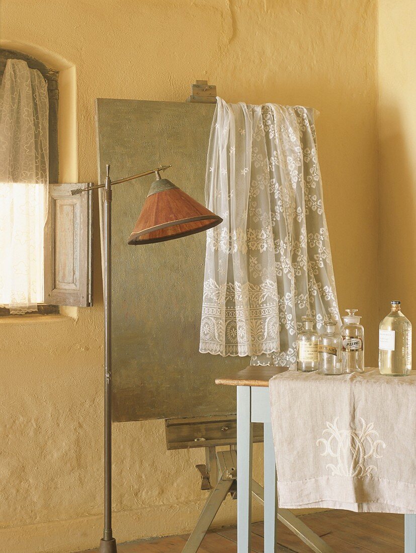 Romantic, vintage-style bathroom with lace curtain hanging over old easel and old apothecary jars