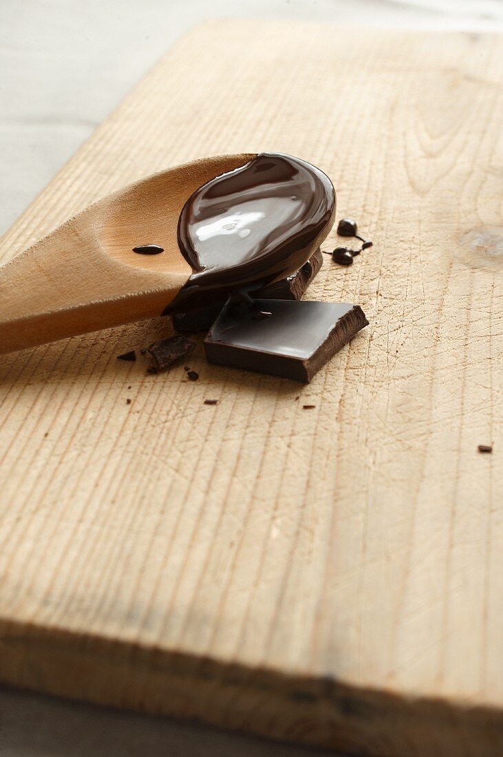 A piece of chocolate and a wooden spoon with melted chocolate