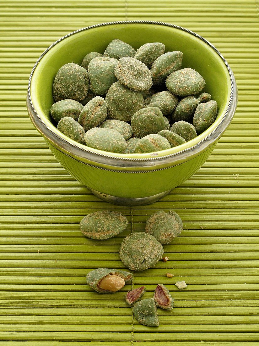 Wasabi peanuts in a green bowl on a bamboo mat