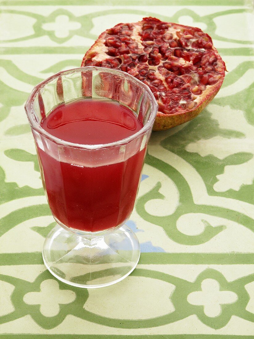 A glass of pomegranate juice with half a pomegranate in the background