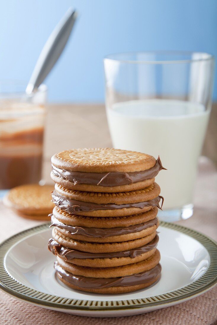 A stack of chocolate sandwich biscuits with a glass of milk in the background