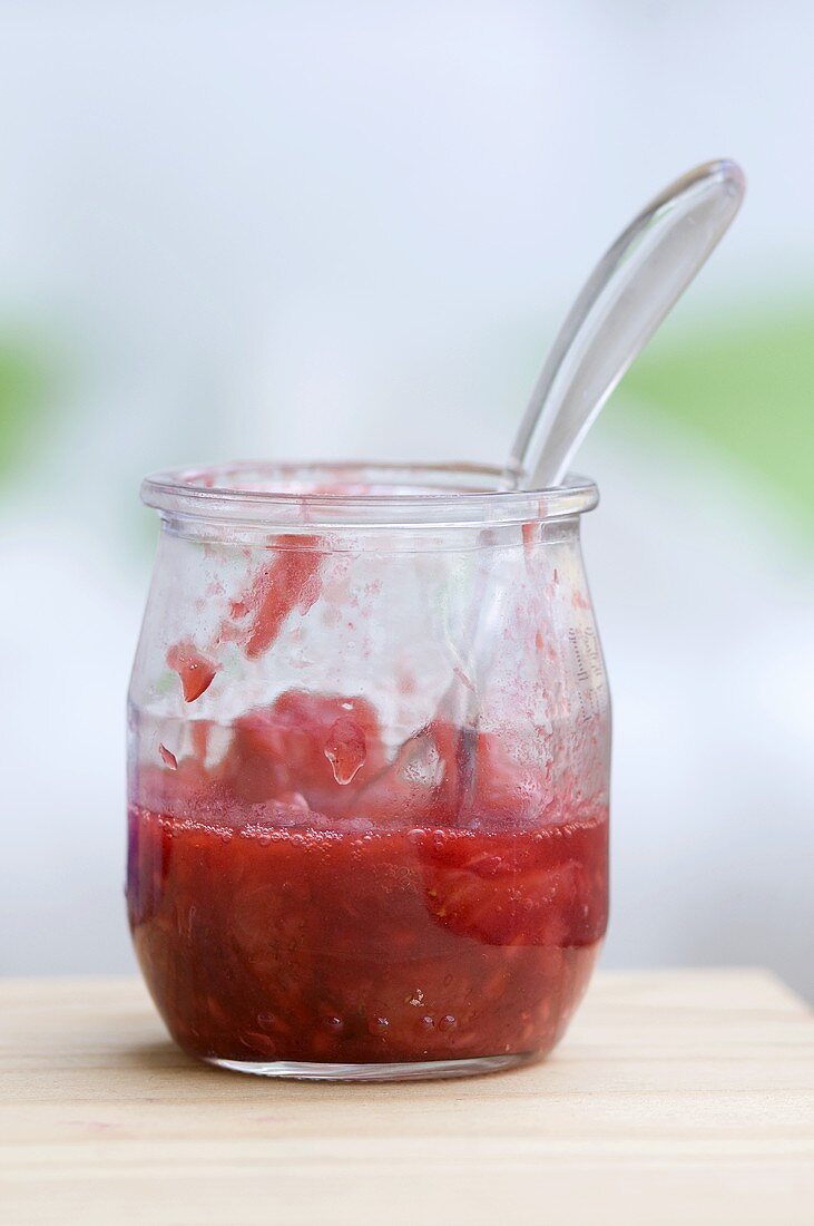 A jar of squashed strawberries and a spoon