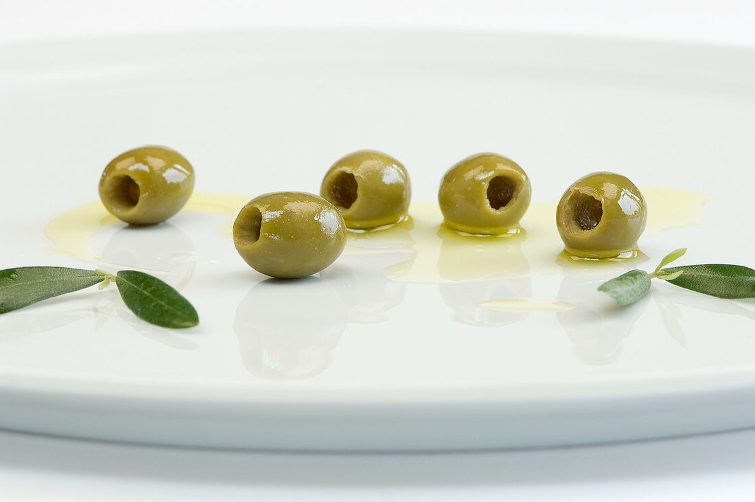 Grüne Oliven mit Blättern und Olivenöl auf Teller