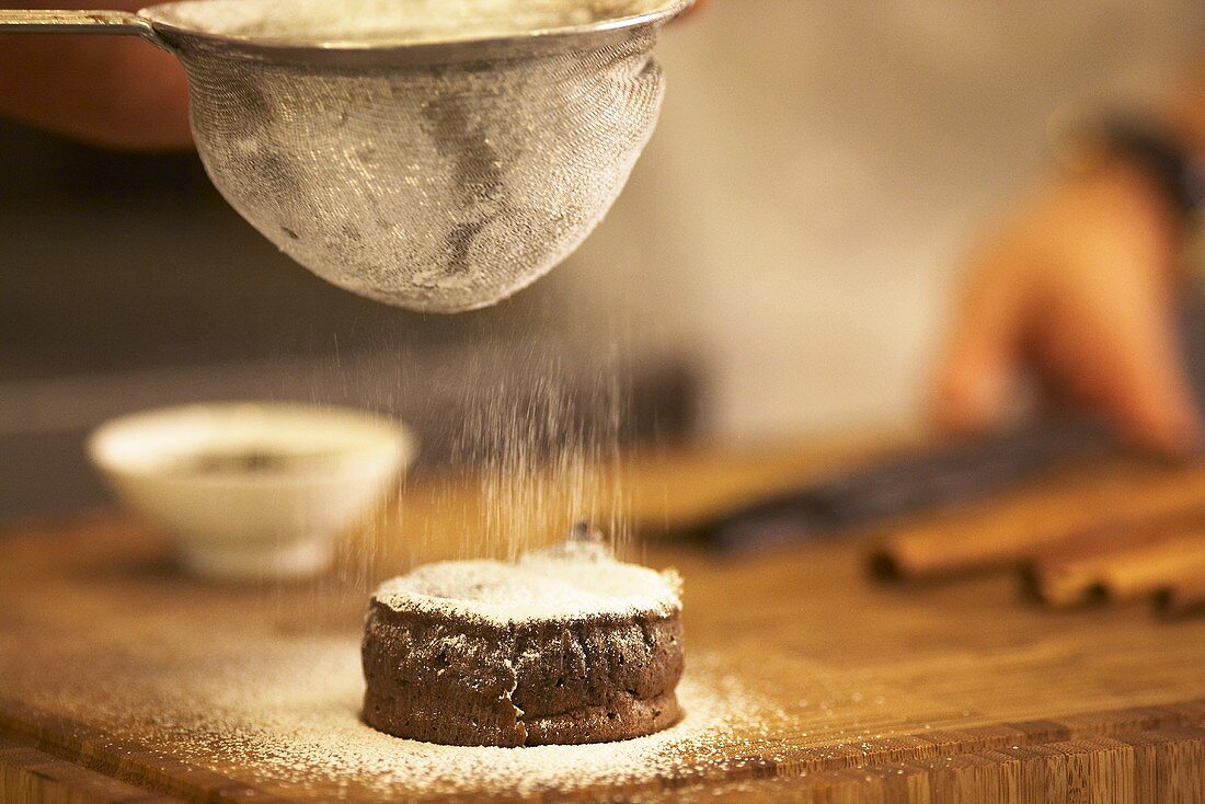 A mini chocolate cake being sprinkled with icing sugar