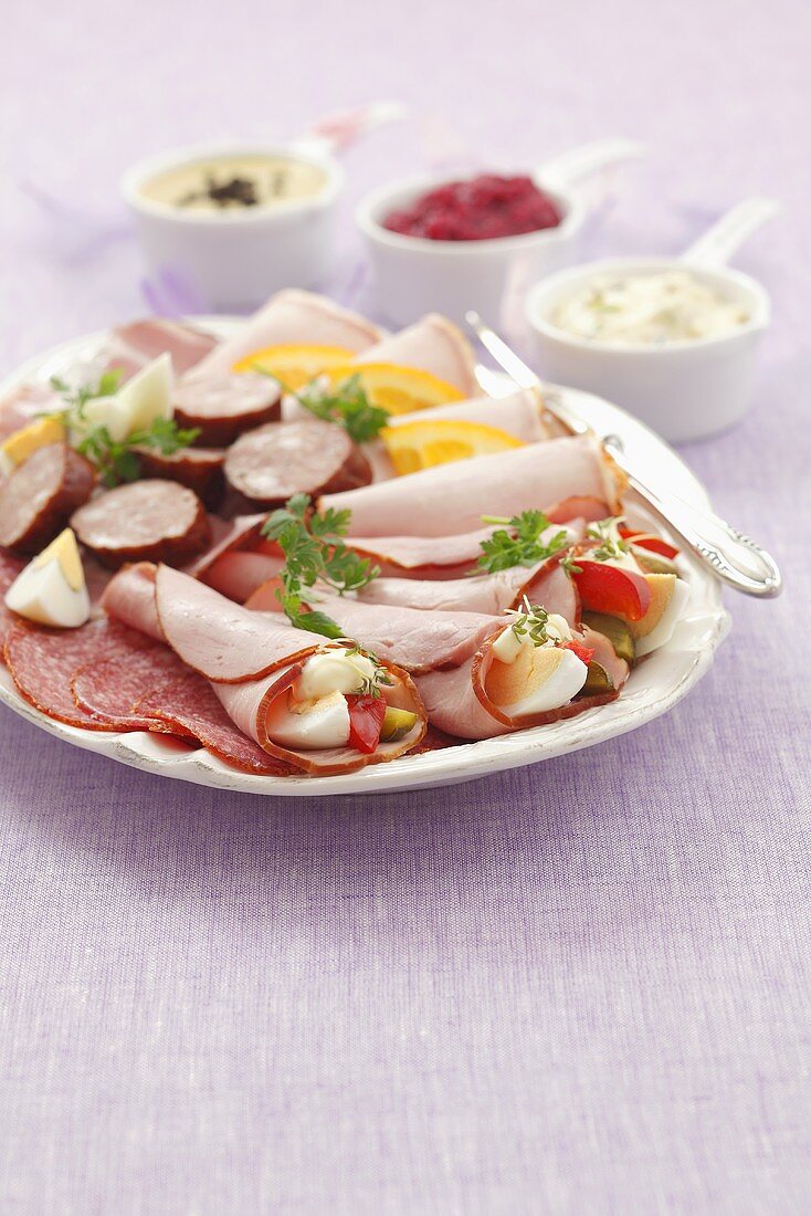 Kalte Platte mit Salami, Schinkenröllchen, Wurst und verschiedenen Saucen