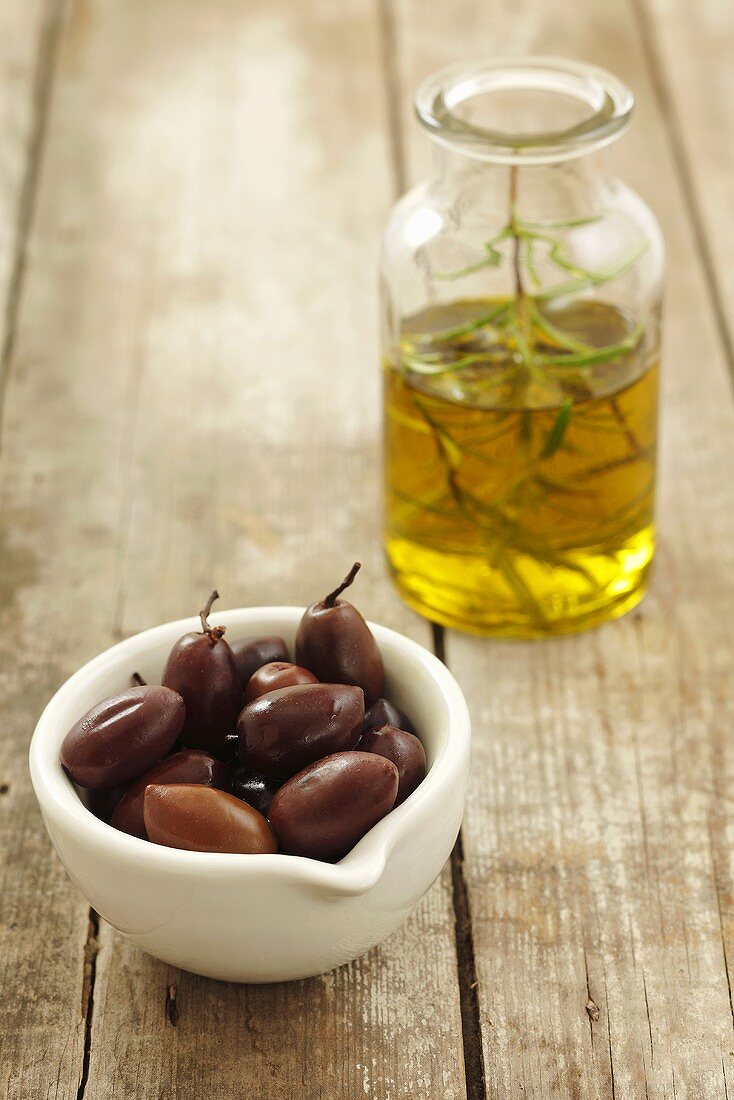 Schwarze Oliven und Olivenöl mit Rosmarin auf Holzuntergrund