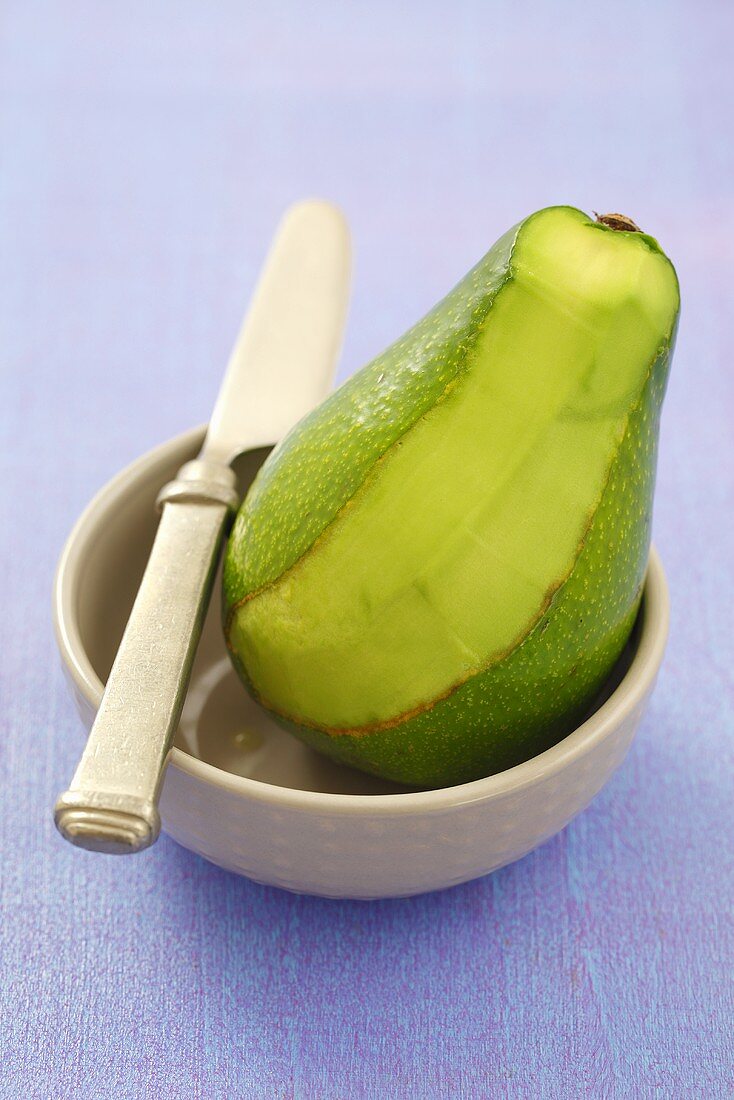 An avocado, sliced, in a bowl with a knife