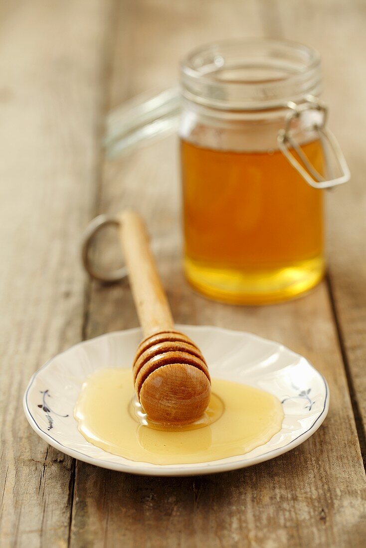 Honey on a plate with a honey spoon with a jar of honey in the background