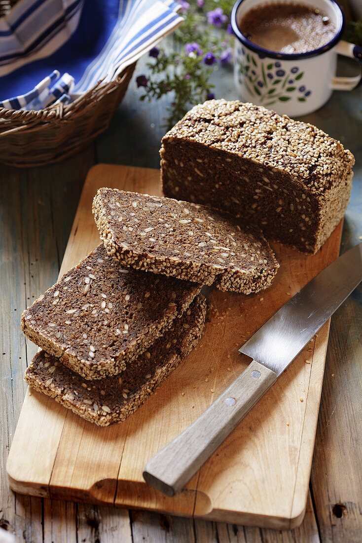 Whole-grain bread with sesame seeds, partly sliced, on board